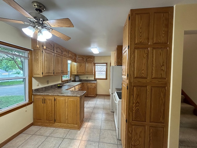 kitchen with light tile patterned floors, a peninsula, white appliances, a sink, and dark countertops