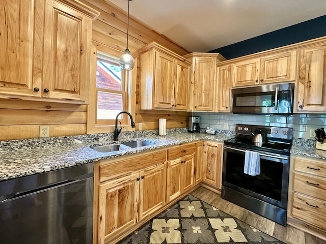 kitchen featuring light stone countertops, light wood-type flooring, stainless steel appliances, sink, and decorative light fixtures