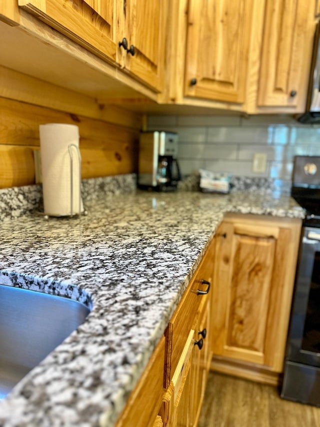 kitchen with hardwood / wood-style flooring, stainless steel electric range, light stone counters, and backsplash