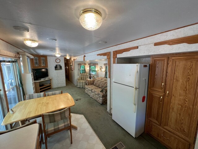 kitchen with tile patterned floors, carpet flooring, freestanding refrigerator, brown cabinetry, and visible vents