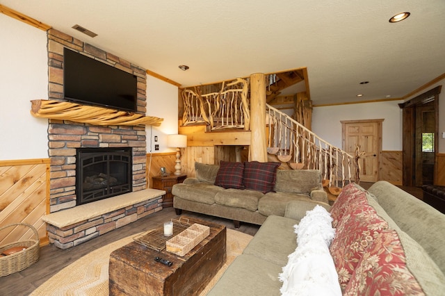 living room with wood walls, crown molding, wood-type flooring, and a stone fireplace