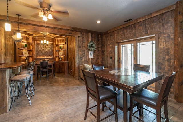 dining space featuring ceiling fan with notable chandelier, wooden walls, and hardwood / wood-style floors