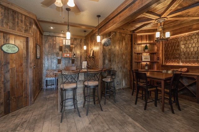 bar with ceiling fan with notable chandelier, wooden walls, hanging light fixtures, and dark wood-type flooring