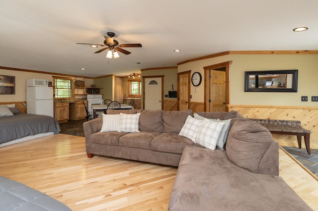 living room featuring wood walls, ceiling fan, light hardwood / wood-style floors, and crown molding