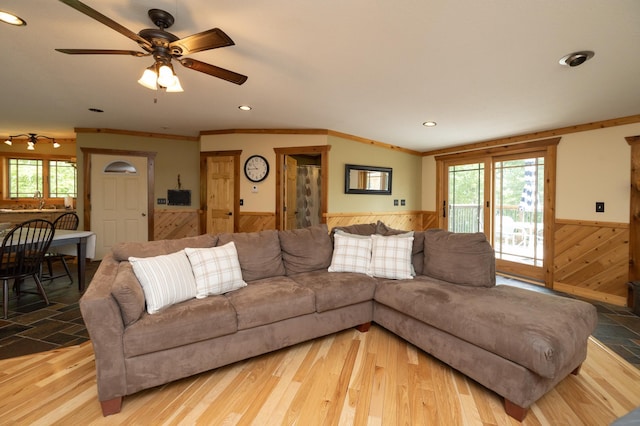 living room with wooden walls, light wood-type flooring, ornamental molding, ceiling fan, and sink