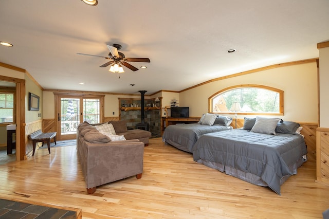 bedroom featuring ceiling fan, light wood-type flooring, crown molding, and a wood stove