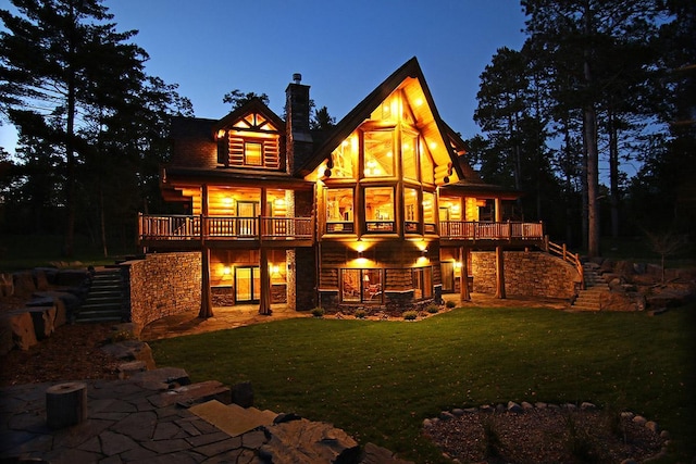 back house at dusk featuring a lawn, a deck, a patio area, and a balcony