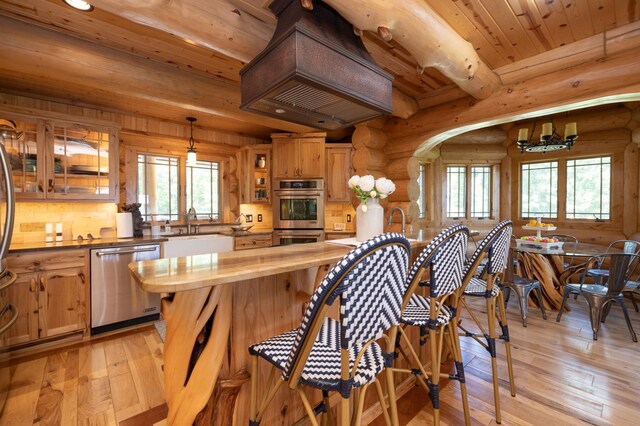 kitchen featuring wood ceiling, stainless steel appliances, rustic walls, decorative light fixtures, and sink