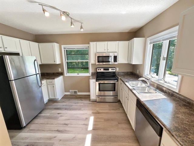 kitchen with a textured ceiling, sink, white cabinets, light hardwood / wood-style flooring, and stainless steel appliances