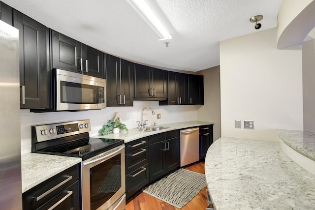 kitchen with light hardwood / wood-style flooring, sink, light stone counters, a textured ceiling, and stainless steel appliances