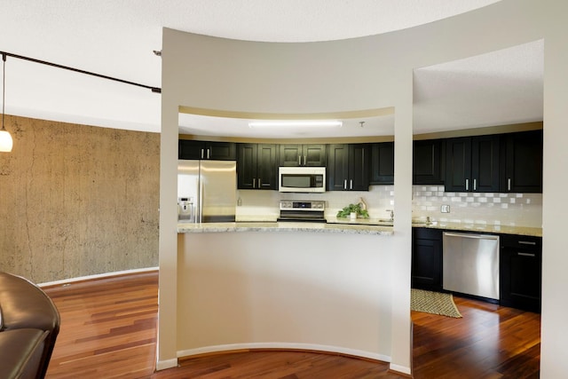 kitchen featuring wood-type flooring, light stone counters, tasteful backsplash, and stainless steel appliances