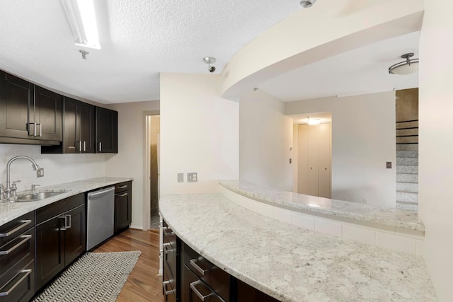 kitchen with light stone countertops, light hardwood / wood-style floors, stainless steel dishwasher, sink, and kitchen peninsula