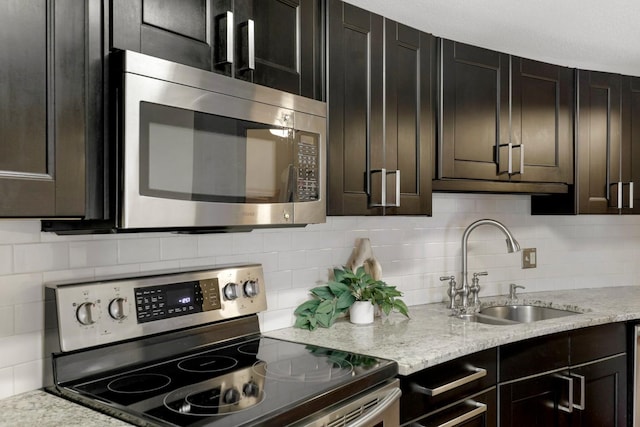 kitchen featuring dark brown cabinets, appliances with stainless steel finishes, sink, light stone countertops, and decorative backsplash