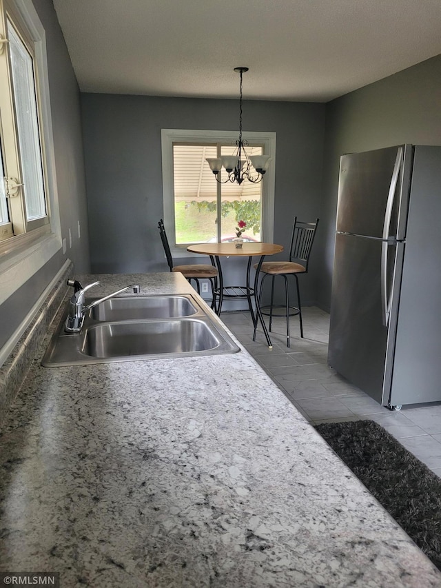 kitchen featuring hanging light fixtures, stainless steel fridge, light tile patterned flooring, sink, and a chandelier