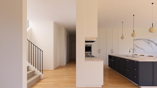 kitchen with appliances with stainless steel finishes, decorative light fixtures, sink, light hardwood / wood-style floors, and a kitchen island with sink