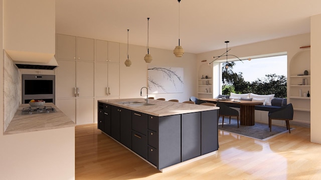 kitchen with stainless steel appliances, sink, decorative light fixtures, a kitchen island with sink, and light hardwood / wood-style flooring