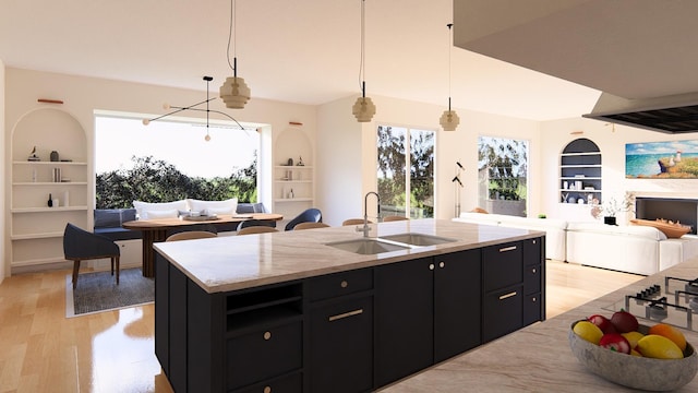 kitchen featuring a center island with sink, light stone countertops, pendant lighting, sink, and light hardwood / wood-style flooring