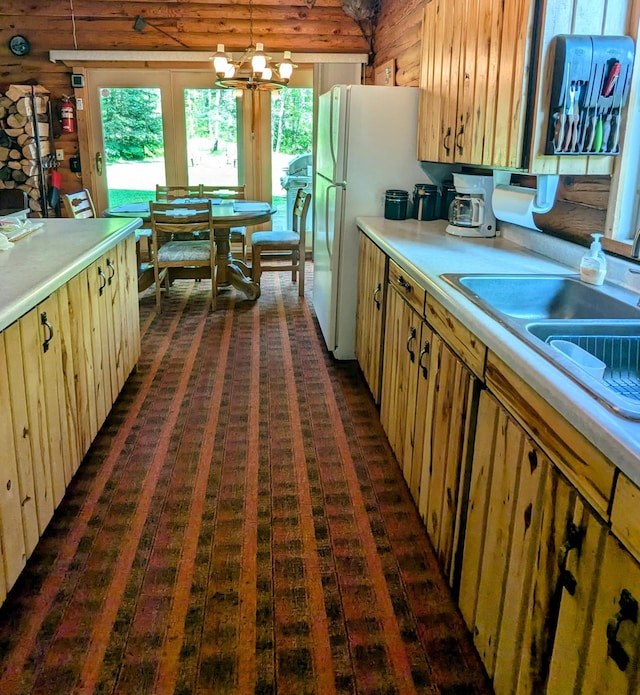 kitchen with wooden walls, sink, pendant lighting, white refrigerator, and a chandelier