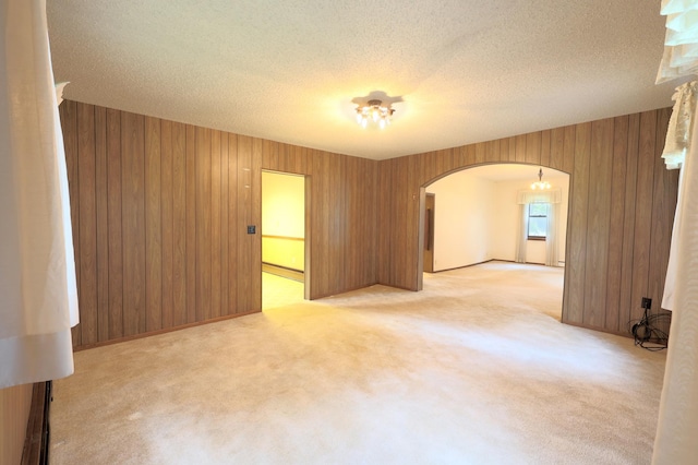 unfurnished room with wood walls, a textured ceiling, and light carpet