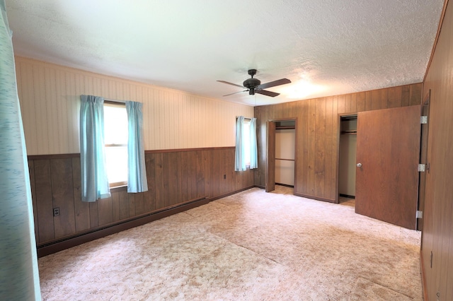 carpeted empty room featuring a textured ceiling, ceiling fan, wood walls, and a baseboard radiator