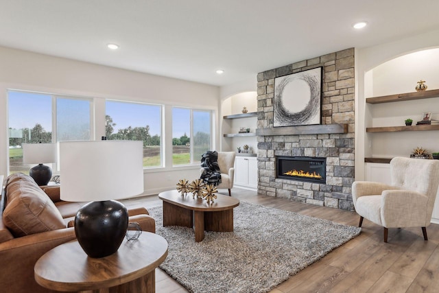 living room featuring built in features, light wood-type flooring, and a stone fireplace