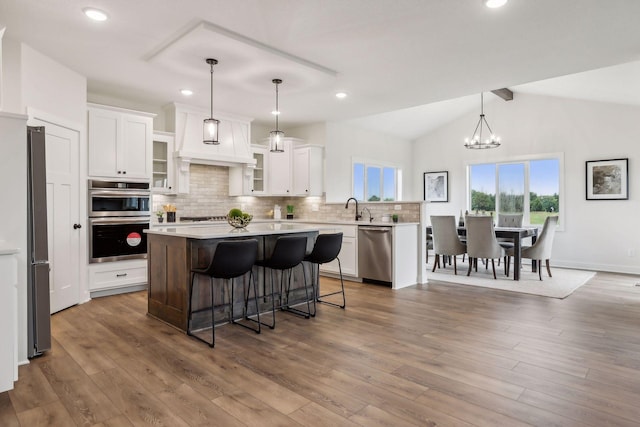 kitchen featuring a center island, appliances with stainless steel finishes, white cabinetry, pendant lighting, and vaulted ceiling