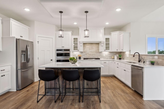 kitchen with white cabinets, appliances with stainless steel finishes, a center island, sink, and hanging light fixtures