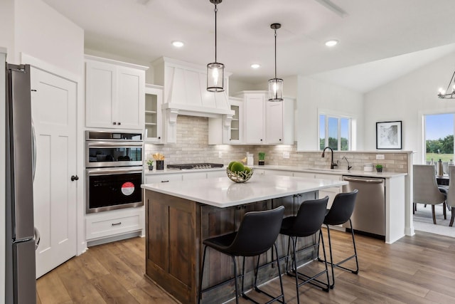 kitchen featuring appliances with stainless steel finishes, a kitchen island, white cabinetry, sink, and vaulted ceiling