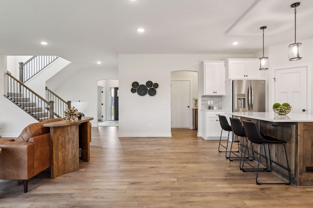 kitchen with decorative light fixtures, stainless steel refrigerator with ice dispenser, white cabinetry, and light hardwood / wood-style floors