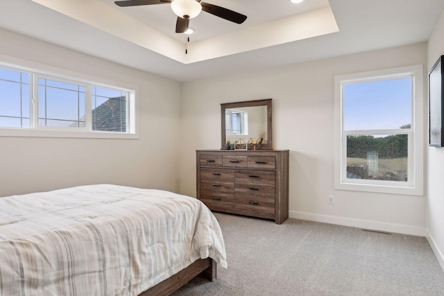 carpeted bedroom with ceiling fan and a raised ceiling