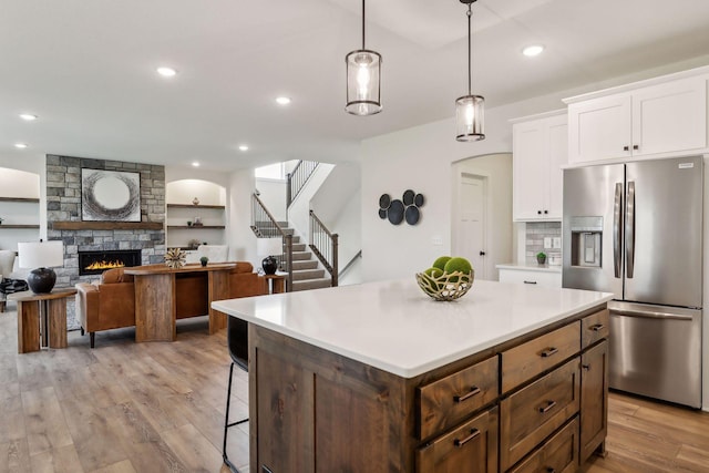 kitchen with a fireplace, stainless steel fridge with ice dispenser, hanging light fixtures, white cabinets, and a kitchen island