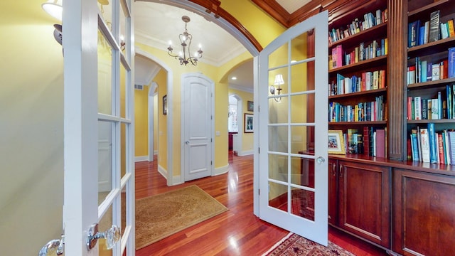 corridor with ornamental molding, french doors, hardwood / wood-style floors, and a notable chandelier