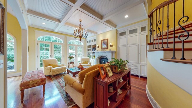 living room with coffered ceiling, beamed ceiling, a notable chandelier, dark wood-type flooring, and ornamental molding