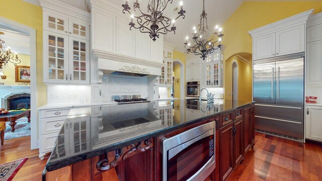 kitchen featuring built in appliances, a kitchen bar, dark hardwood / wood-style flooring, premium range hood, and a center island with sink