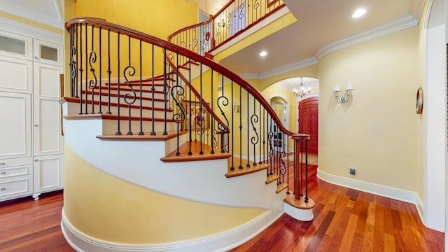 stairway with ornamental molding, a notable chandelier, and wood-type flooring