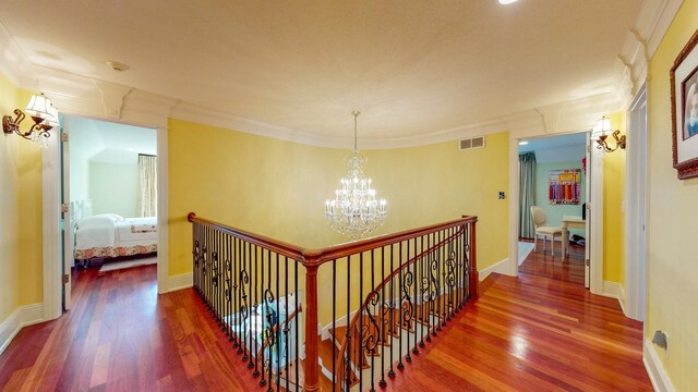 corridor with ornamental molding, an inviting chandelier, and dark hardwood / wood-style floors