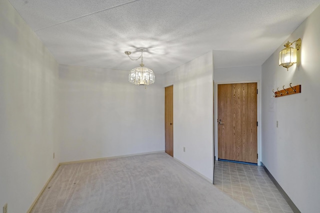 empty room with light colored carpet, a chandelier, and a textured ceiling