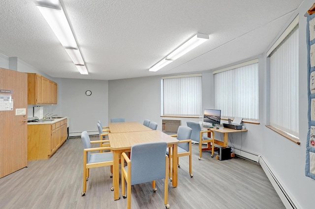 dining area with a baseboard heating unit, light wood-type flooring, and a textured ceiling