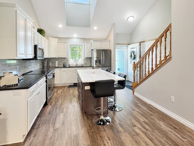 kitchen featuring hardwood / wood-style floors, appliances with stainless steel finishes, backsplash, and vaulted ceiling