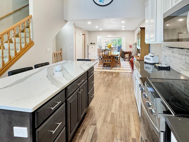 kitchen featuring light wood-type flooring, white cabinetry, a kitchen island, decorative backsplash, and appliances with stainless steel finishes