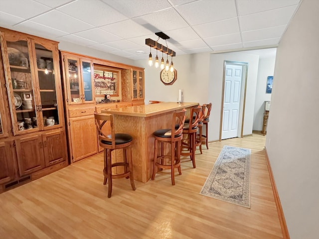 dining space with bar area, a paneled ceiling, and light hardwood / wood-style floors