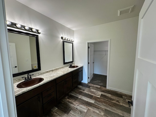 full bath featuring wood finished floors, double vanity, a sink, and visible vents
