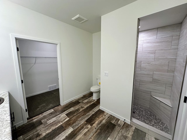 full bath featuring tiled shower, visible vents, toilet, and wood finished floors