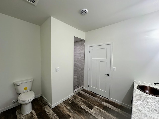 full bathroom with baseboards, a tile shower, toilet, and wood finished floors