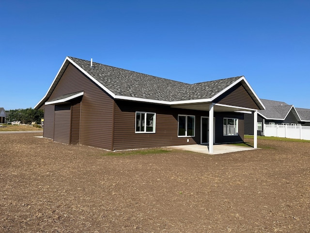 rear view of house with fence, a patio, and roof with shingles