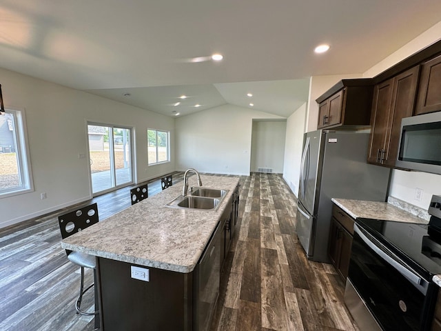 kitchen with appliances with stainless steel finishes, sink, dark wood-type flooring, a kitchen breakfast bar, and a kitchen island with sink