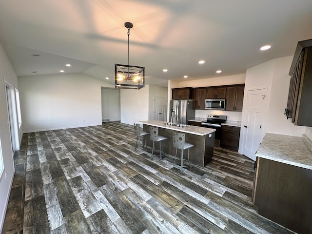 kitchen with vaulted ceiling, dark hardwood / wood-style floors, a center island with sink, appliances with stainless steel finishes, and sink