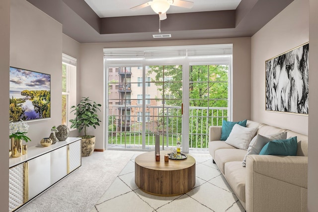 carpeted living room with ceiling fan, plenty of natural light, and a raised ceiling