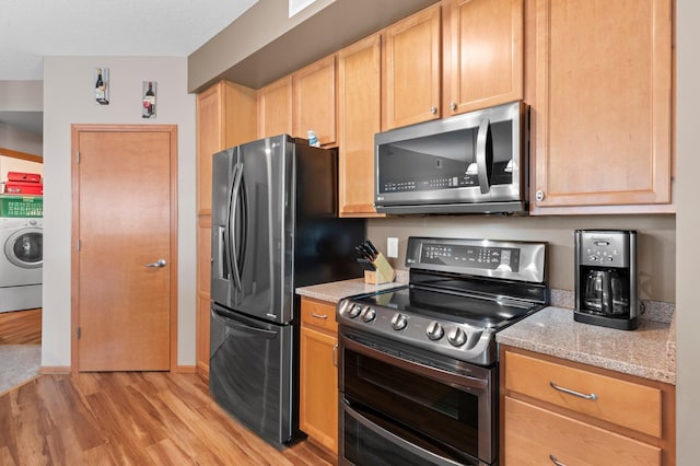 kitchen with stainless steel appliances, light stone counters, light hardwood / wood-style flooring, light brown cabinetry, and washer / dryer