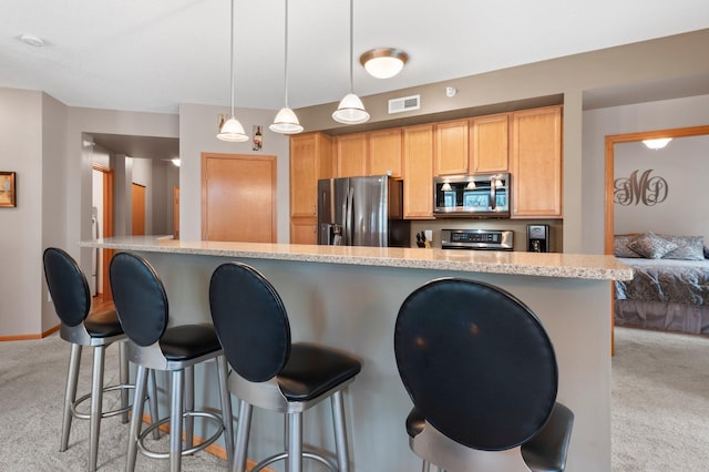 kitchen featuring light brown cabinets, appliances with stainless steel finishes, decorative light fixtures, and light carpet